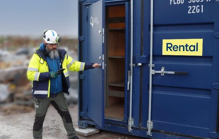 En person i varseljacka och skyddshjälm öppnar dörren till en blå förrådscontainer märkt med